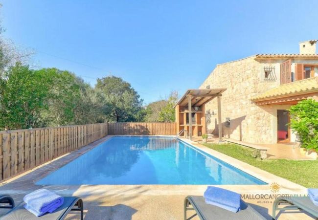 Piscina vallada con zona de barbacoa junto a una villa de piedra de estilo mallorquín.